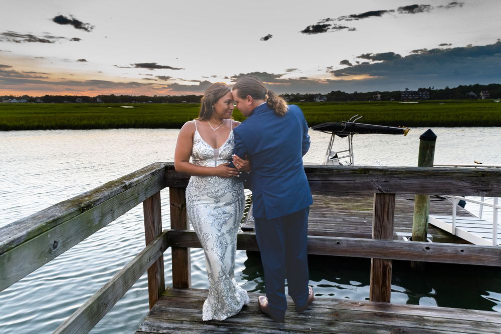Evening wedding portrait on waterfront dock with dramatic sunset sky over marsh.