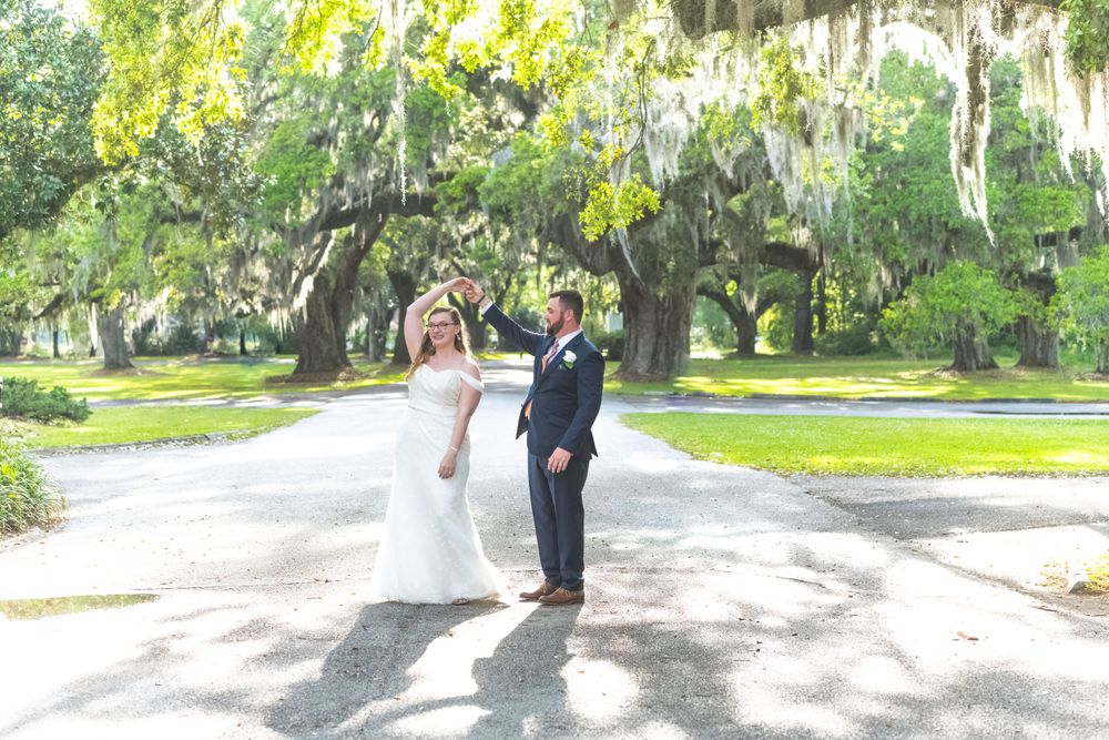 Wedding couple poses on tree-lined path with Spanish moss hanging from branches.