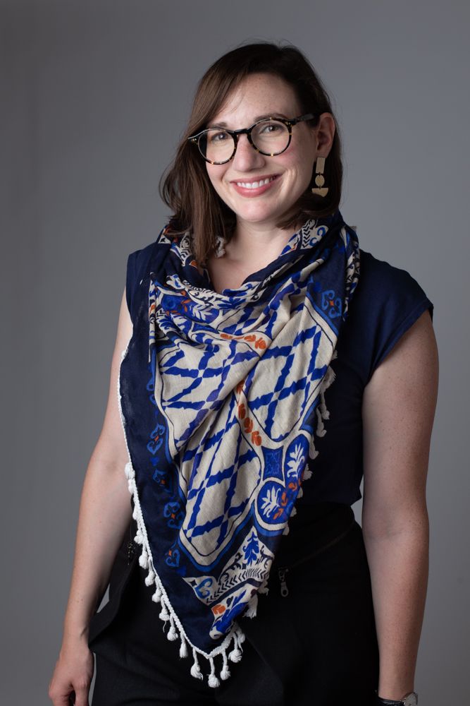 Portrait featuring glasses, a patterned blue scarf, and a navy sleeveless top.