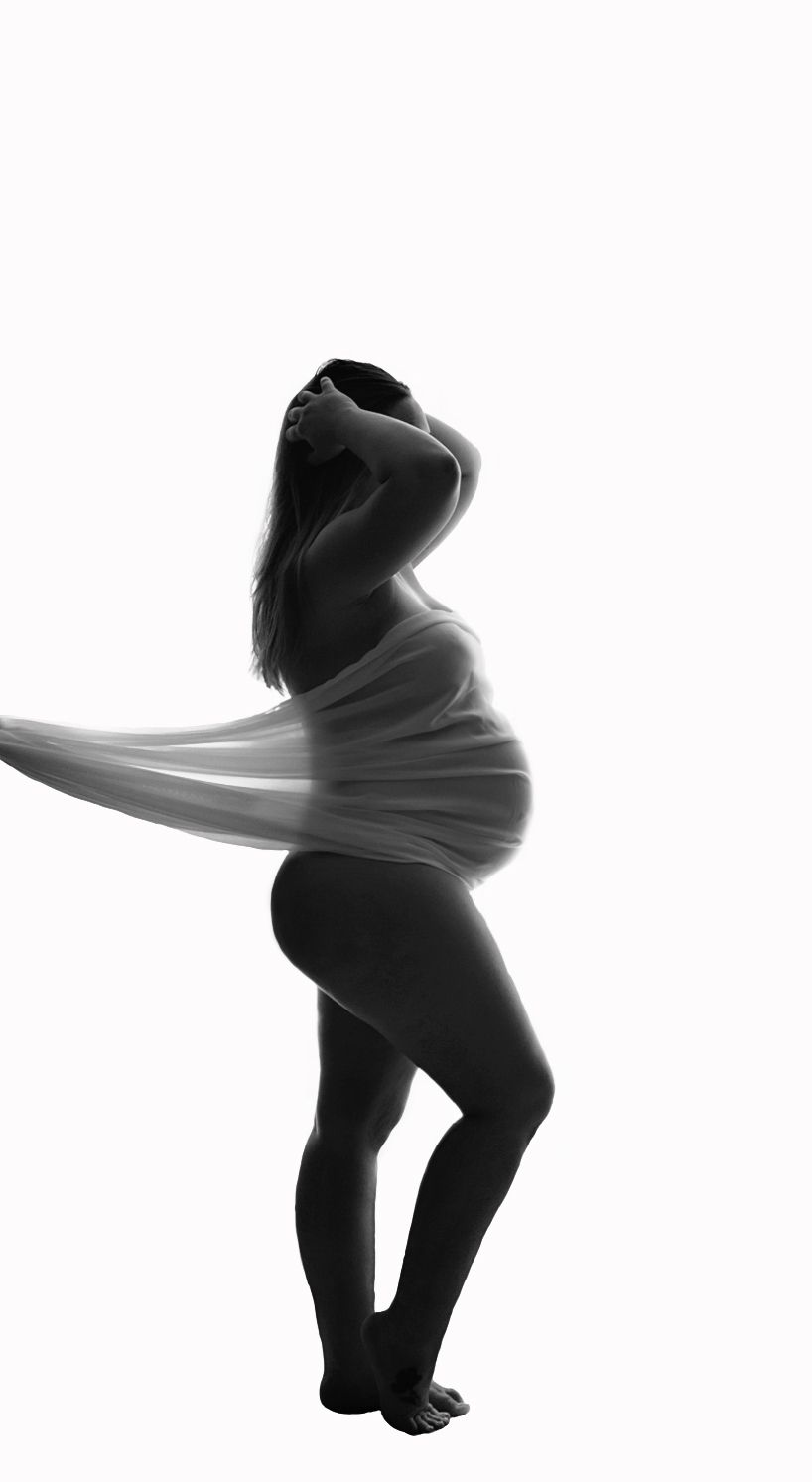 Kaitlyn pregnant in front of white backdrop with sheer material draped over her belly