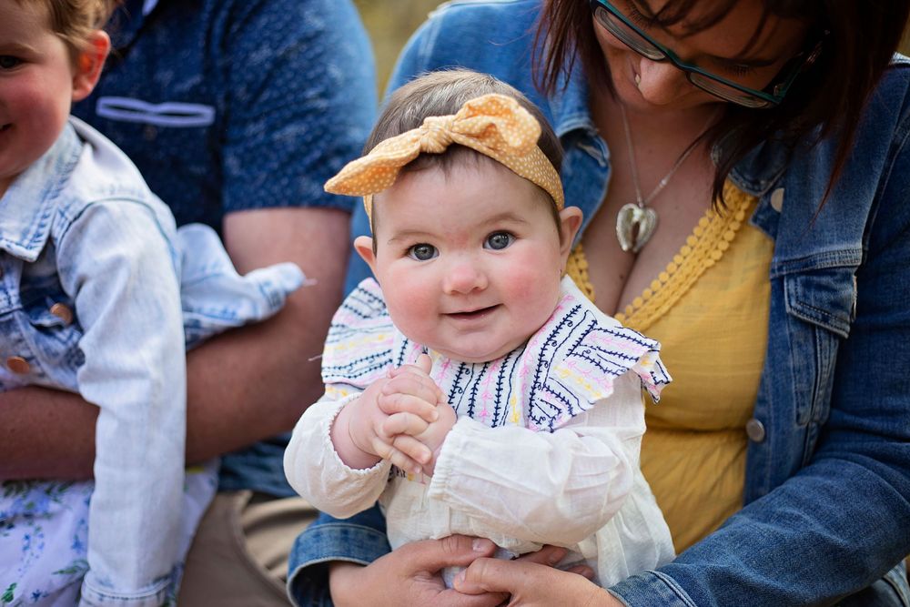 little girl sitting on her mums lap clapping her hands with a yellow bow