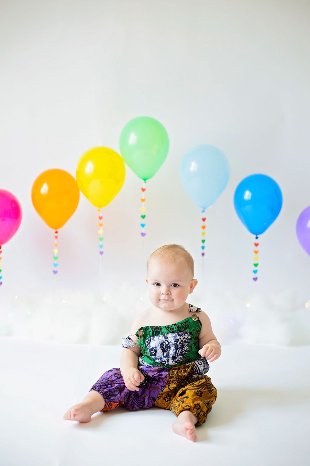 Noah sitting in front of rainbow balloons for his confetti cake smash wearing bright colours