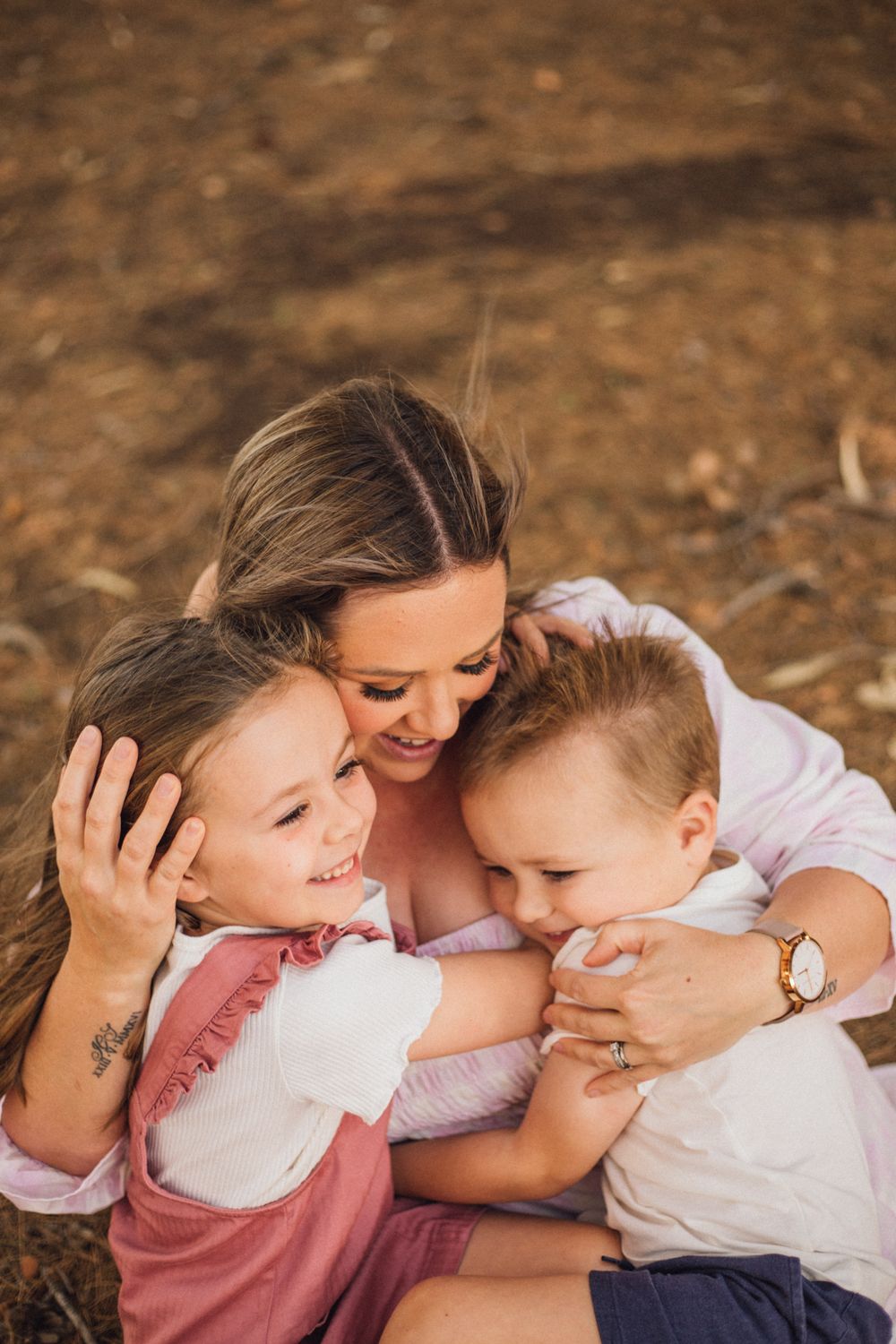mother cuddling her two children really close with smiles on their faces