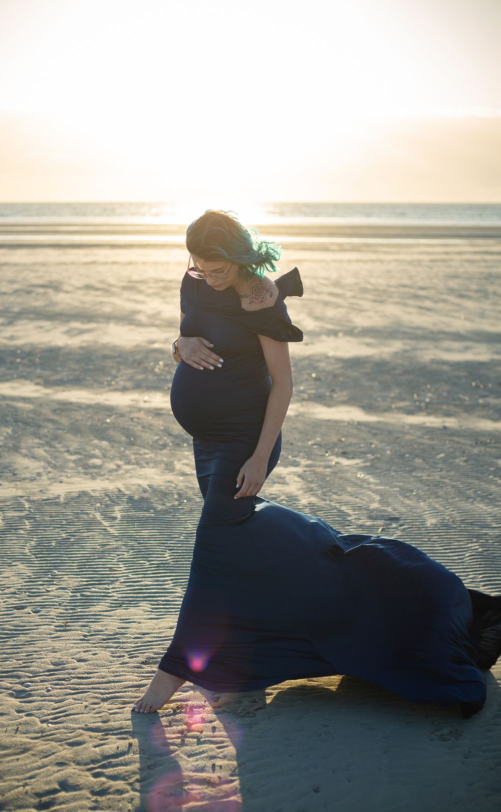 Erin, pregnant and wearing blue to match her hair cradling her belly on Wallaroo North Beach