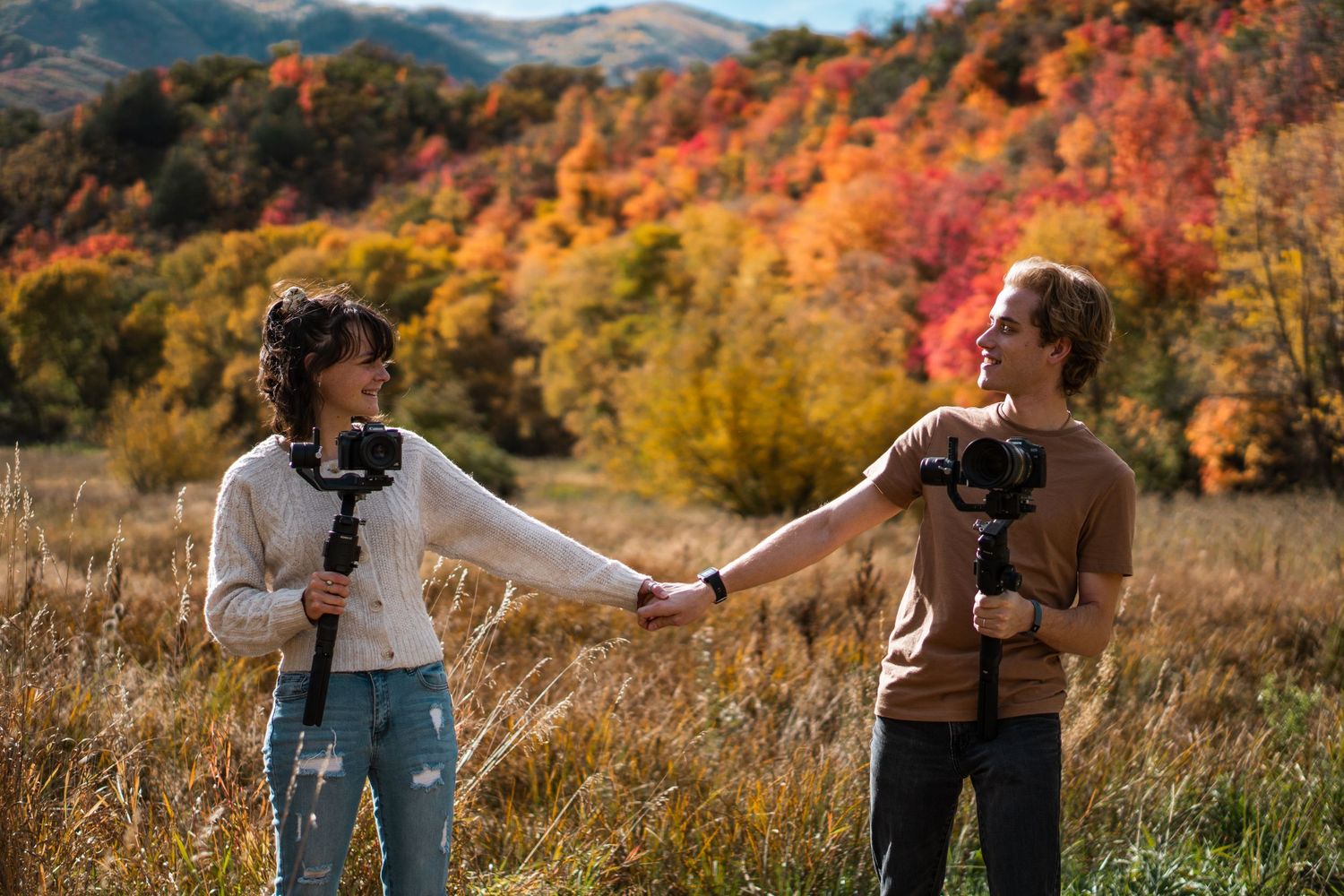 Husband and wife in the mountains during fall holding hands and holding their video and photography cameras