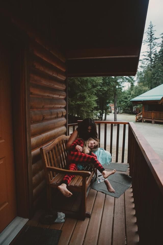 A cozy log cabin porch with wooden rocking chairs overlooking a forest setting.