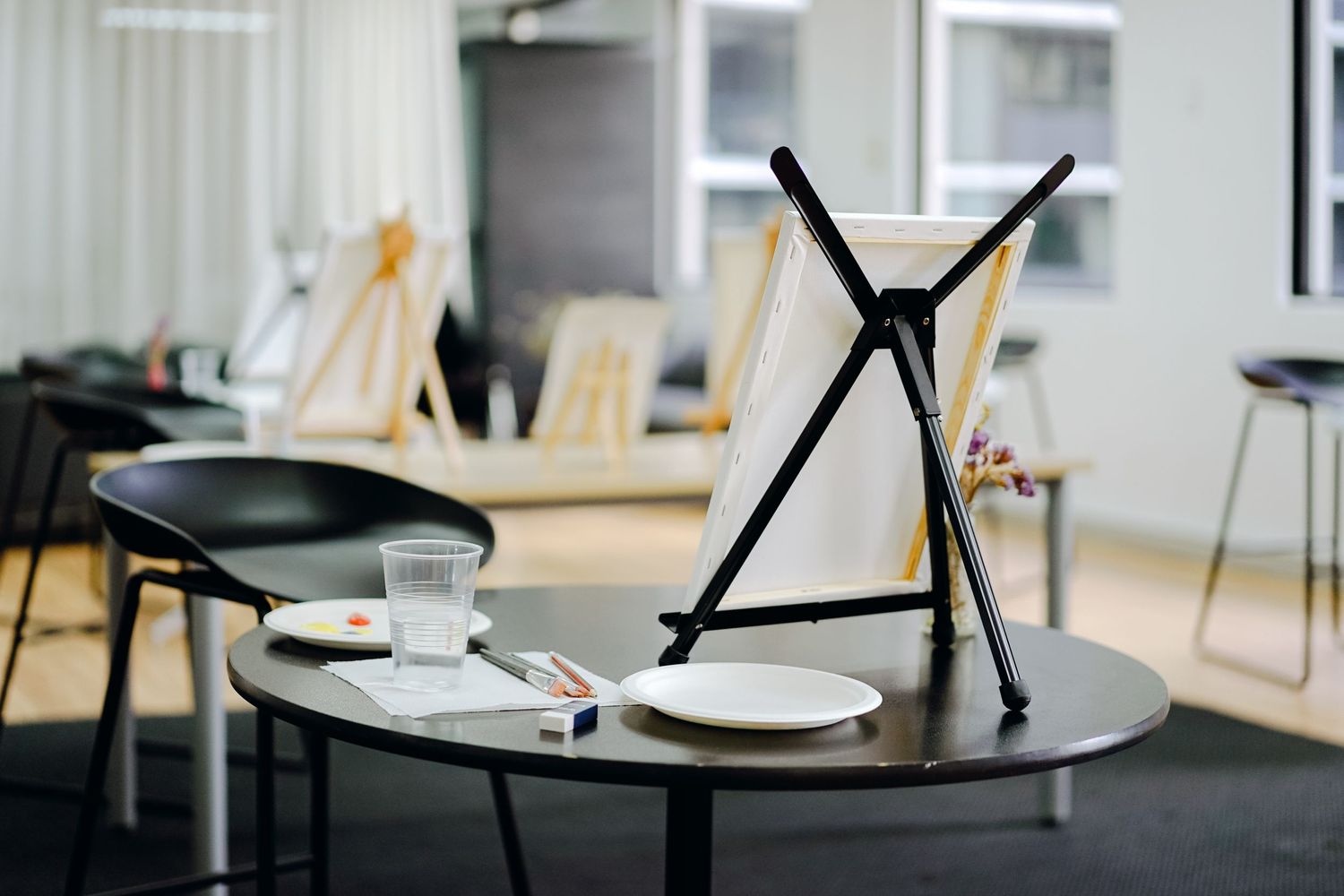 Minimalist round table with black tripod stand and empty plates in modern office setting.