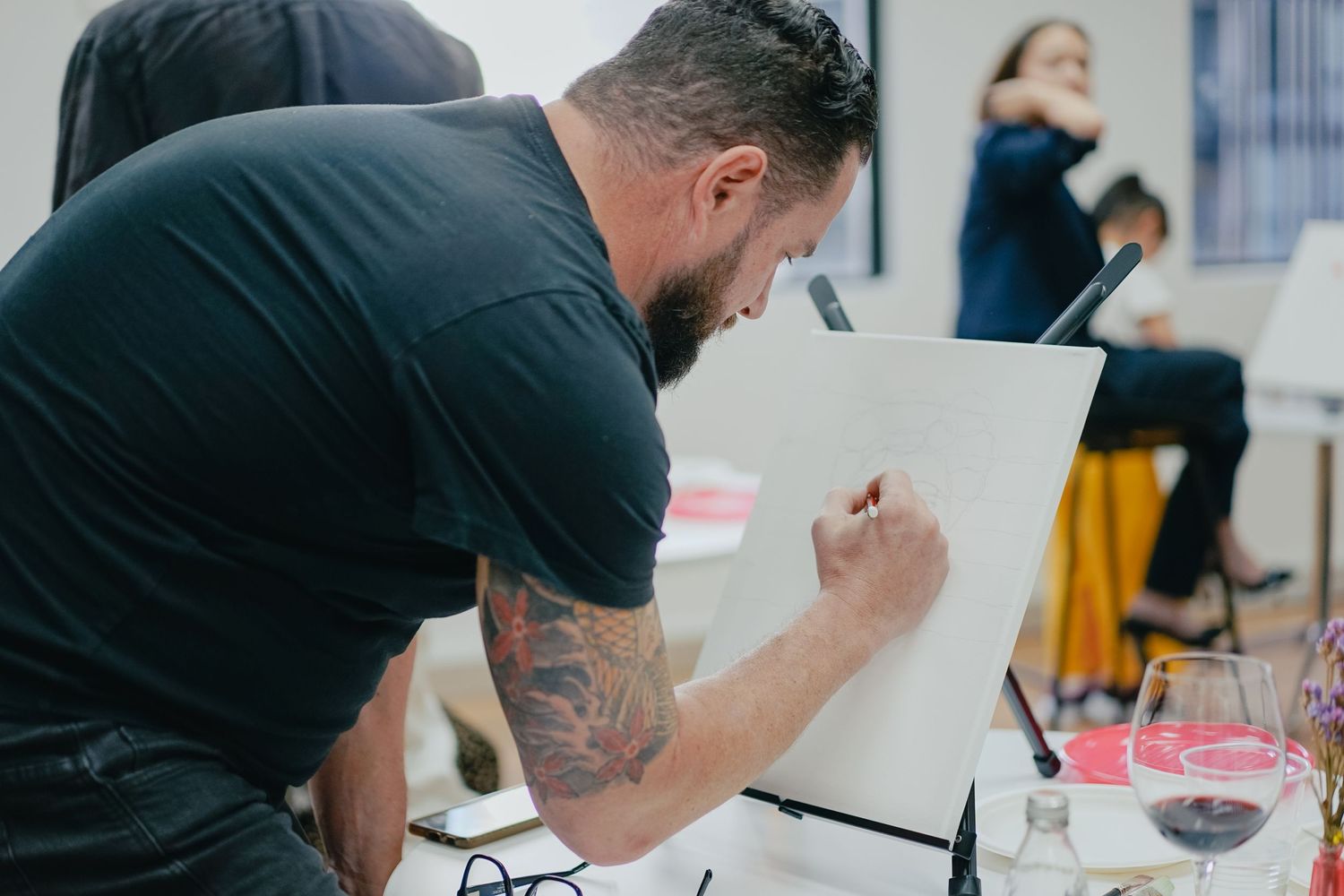 Artist in black shirt with tattoos concentrating while sketching at an easel.