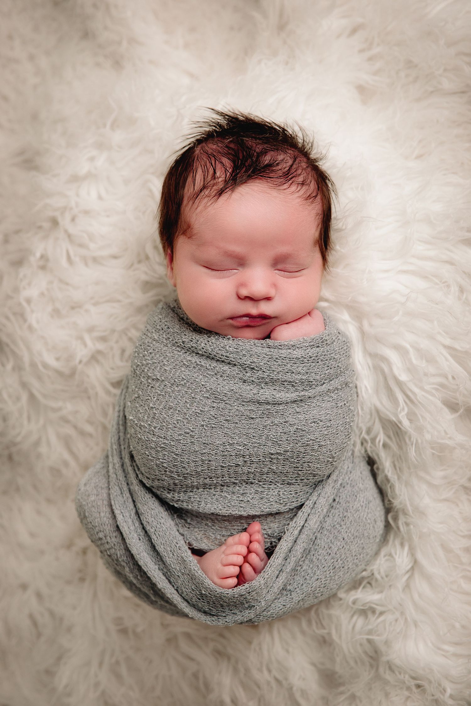 baby boy wrapped in baby blue and laying on white fur blanket