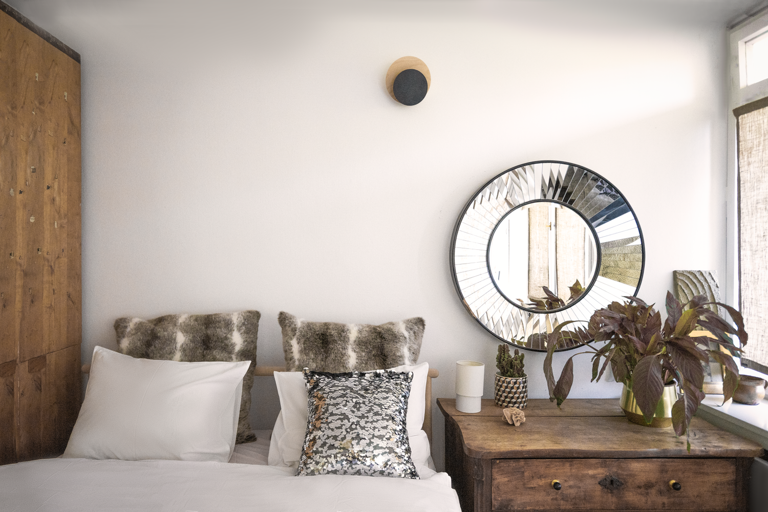 Cozy bedroom corner with round mirror, fur pillows and wooden furniture.