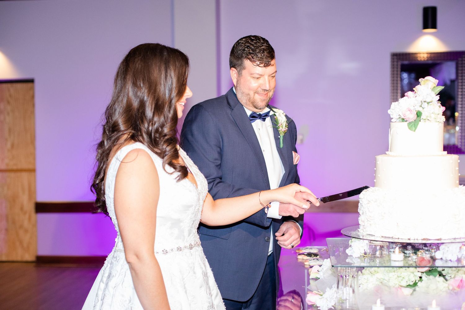 A couple cuts their elegant white wedding cake decorated with fresh flowers at their reception.