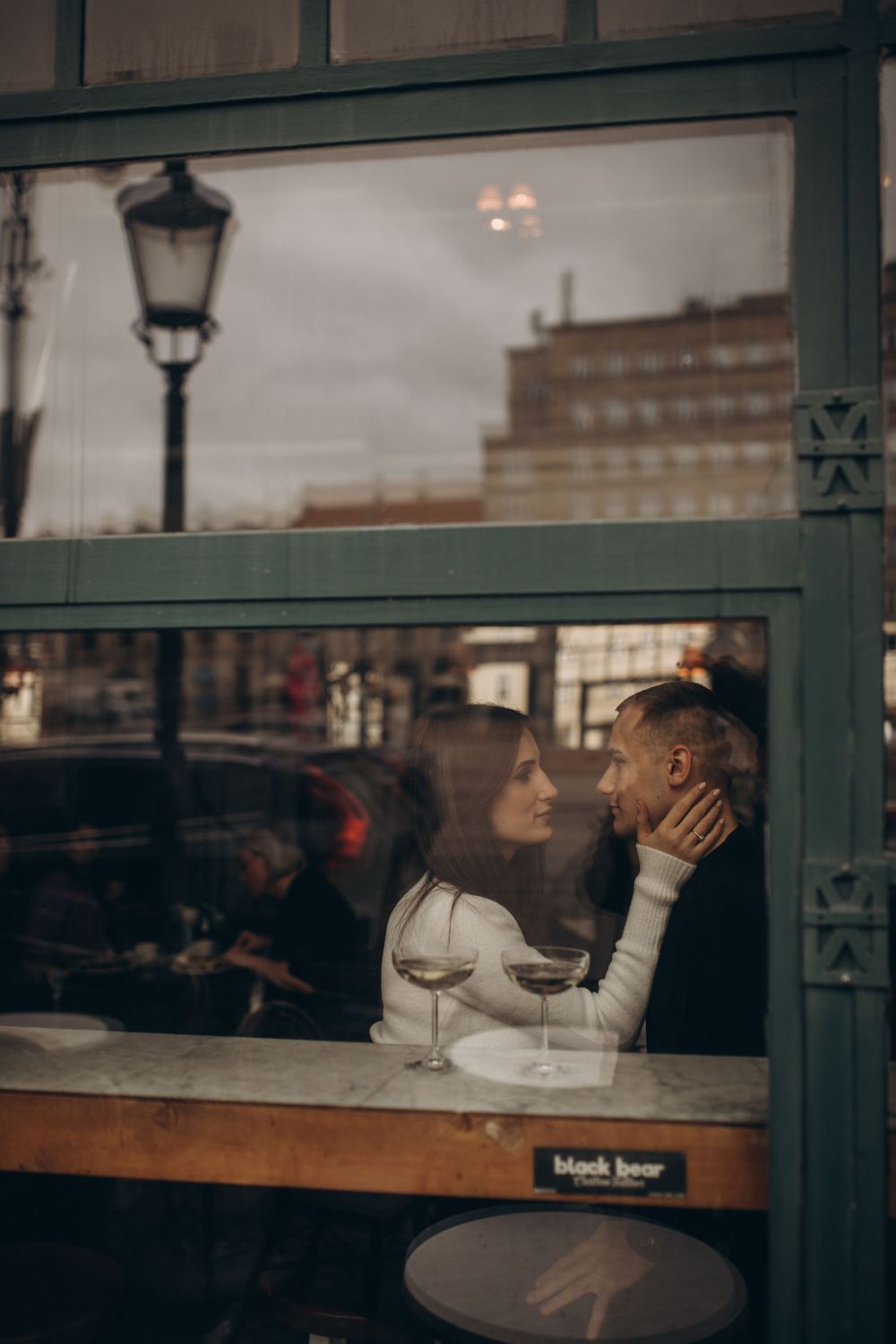 Romantic dinner date through cafe window with wine glass and street lamp.