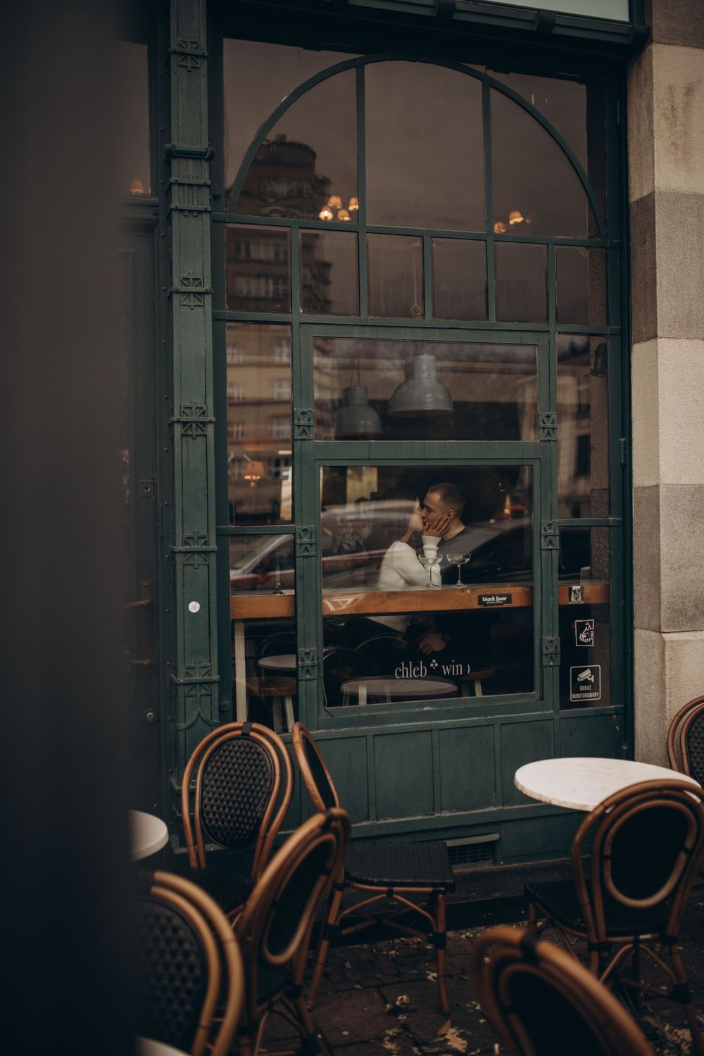 Cozy cafe scene through arched window with bistro chairs in foreground.