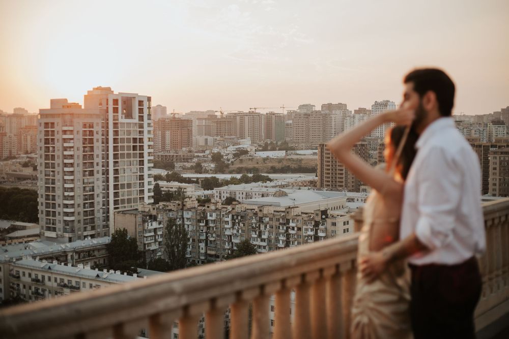 Couple overlooking cityscape from balcony during golden sunset hour.