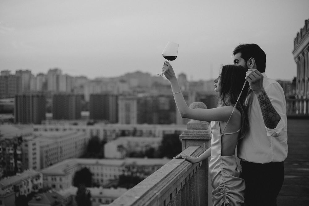 Black and white photo of couple sharing wine while overlooking urban cityscape at dusk.