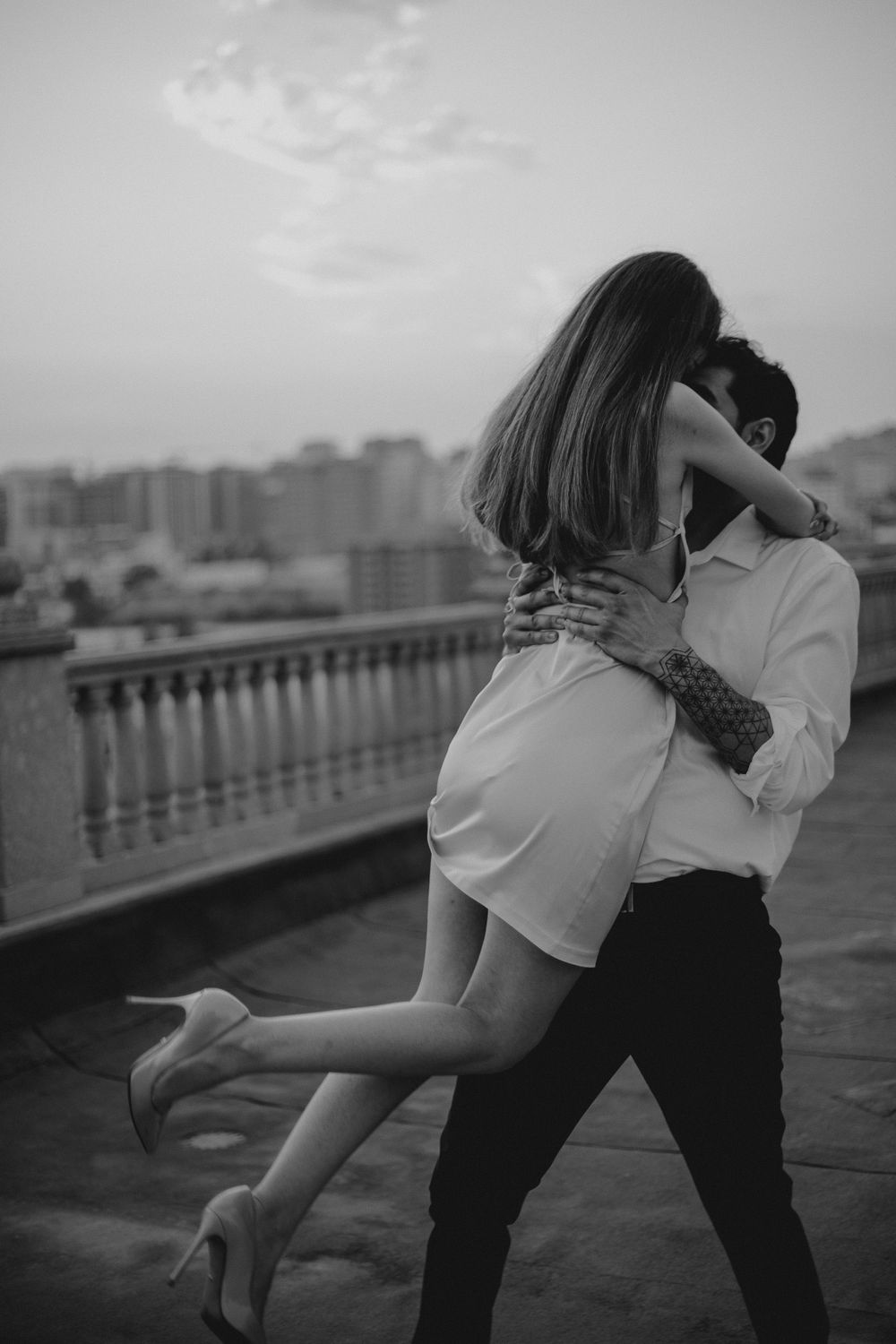 Intimate dance pose captured on balcony overlooking city buildings.