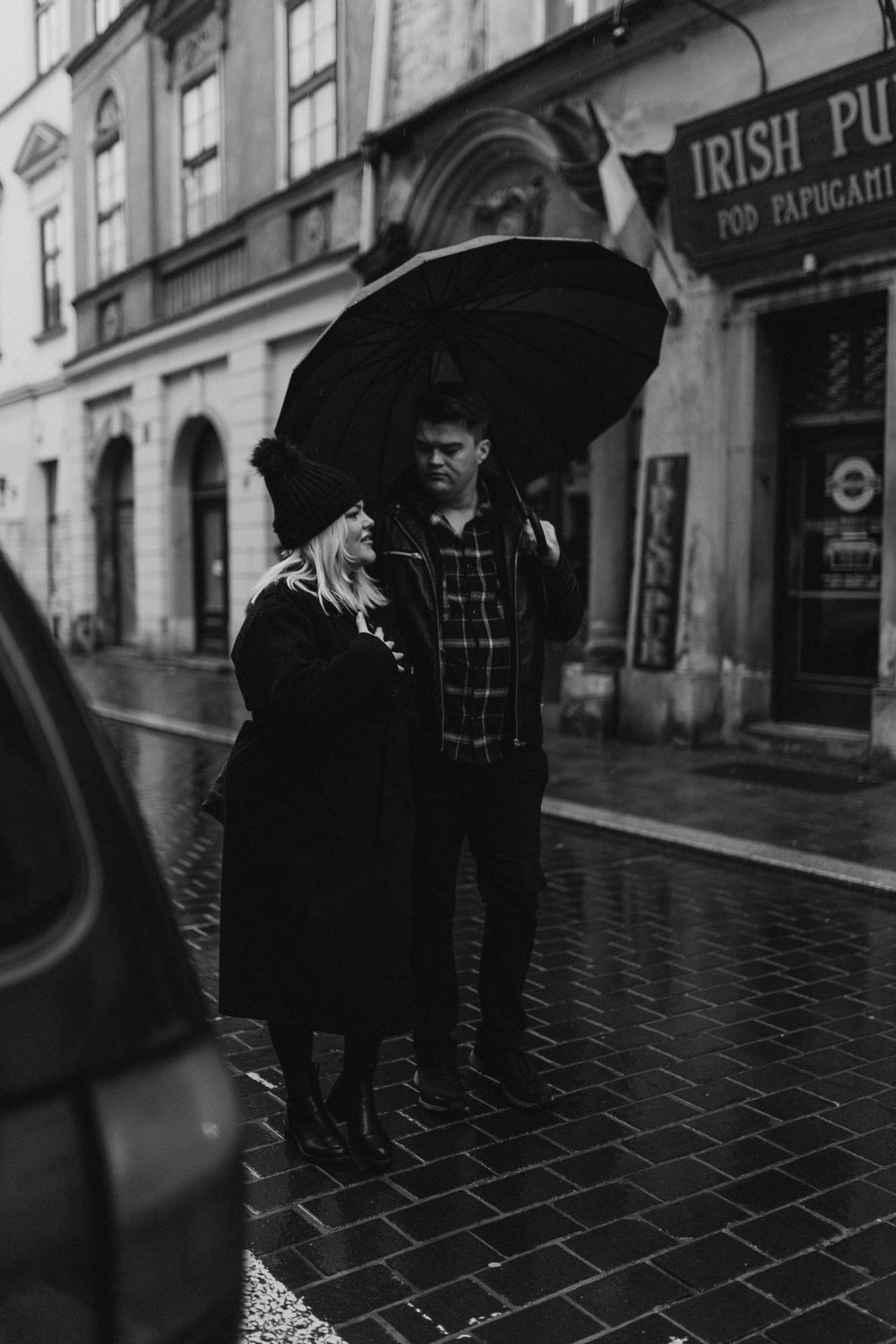 Couple sharing umbrella outside Irish pub on rainy cobblestone street.