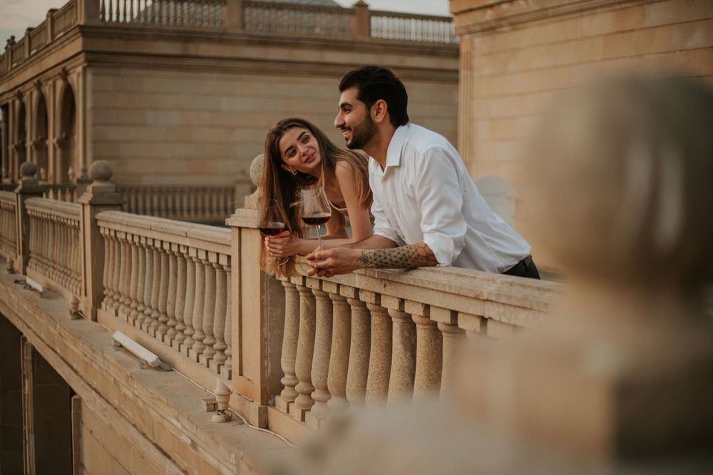 Couple sharing romantic moment while leaning on balcony railing at golden hour.