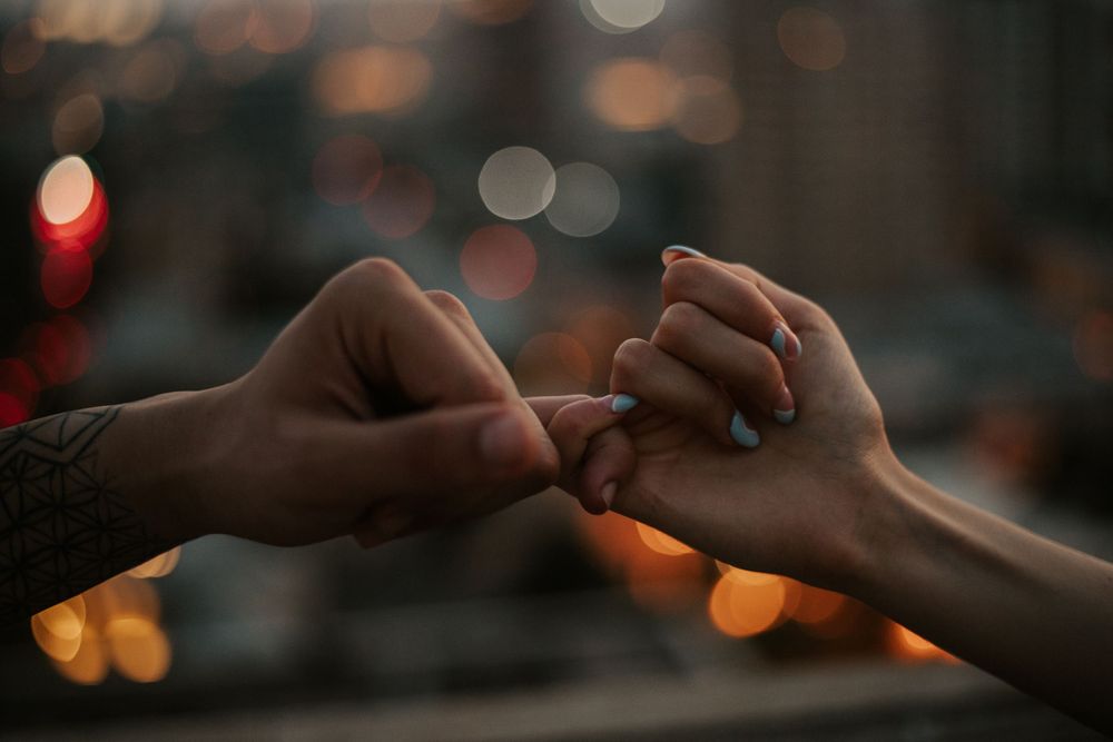 Close-up of hands reaching toward each other against blurred bokeh lights background.