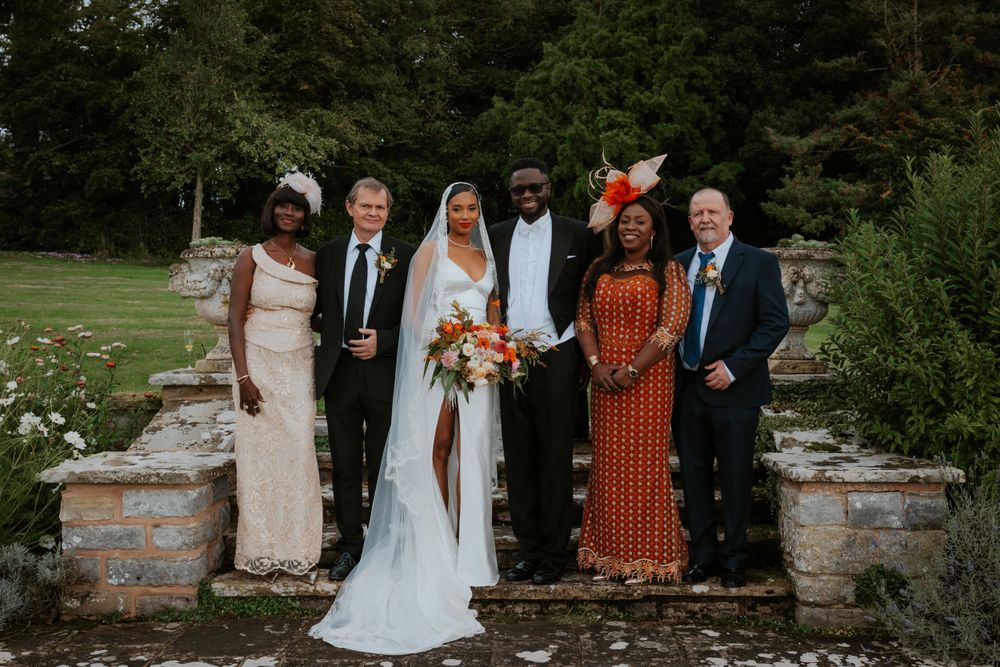 Wedding party poses for formal group photo in front of stone garden wall.