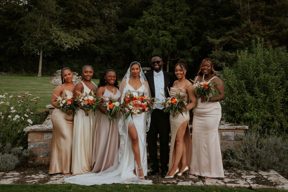 Wedding party in blush and white gowns poses on stone steps in garden setting.