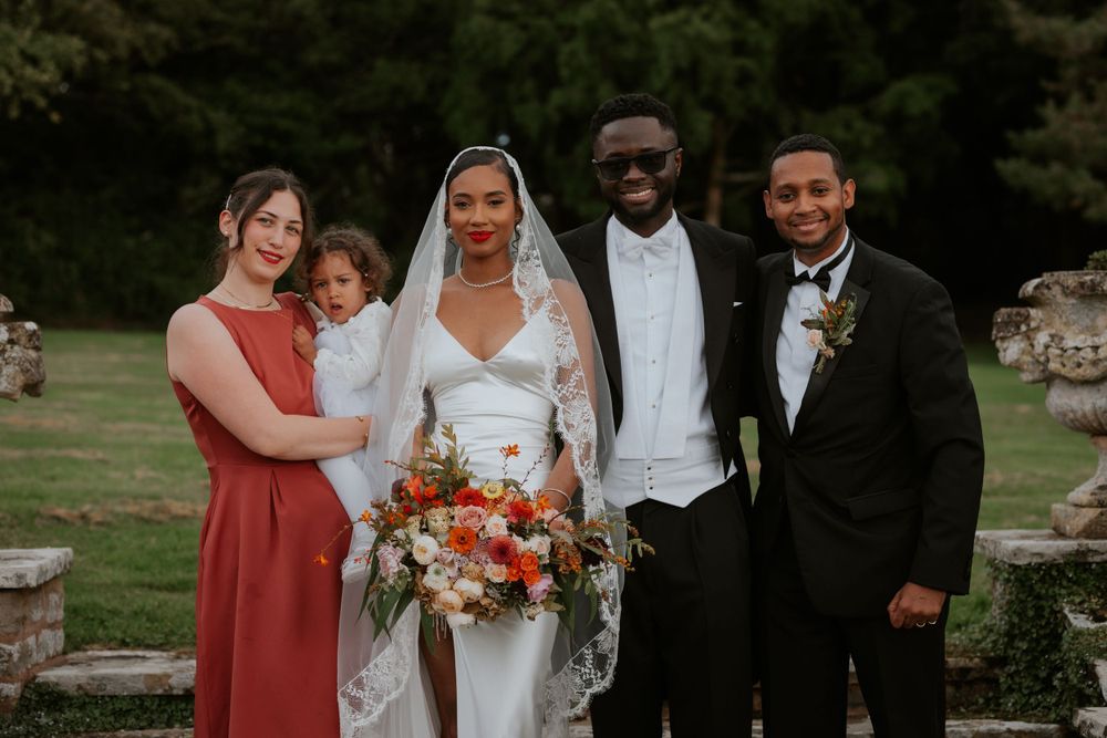 Intimate wedding party portrait against stone wall backdrop in garden setting.
