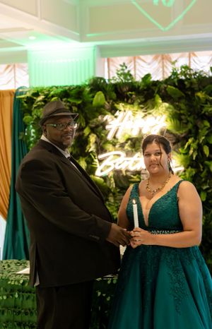 Couple in elegant attire dancing and smiling at formal event with green lighting.