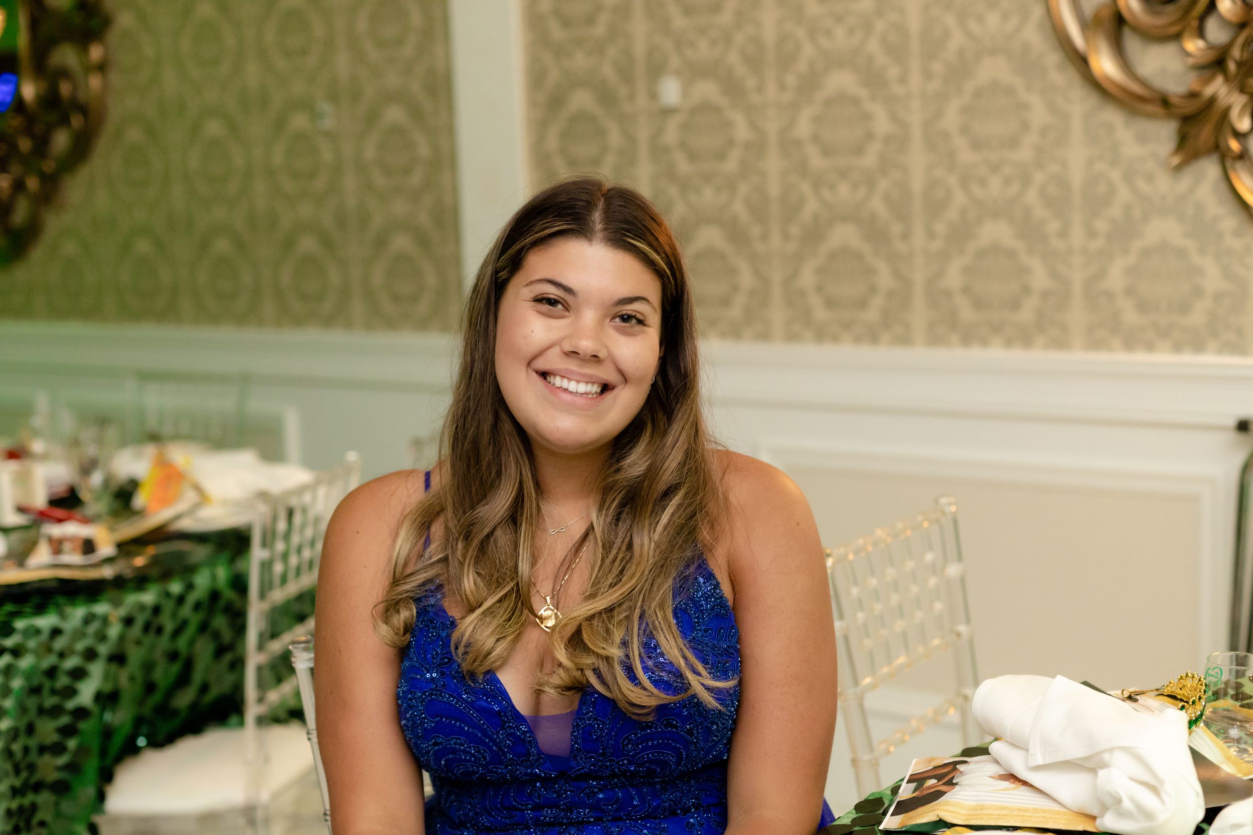 Guests in formal attire smile during a celebration in an elegantly decorated room.