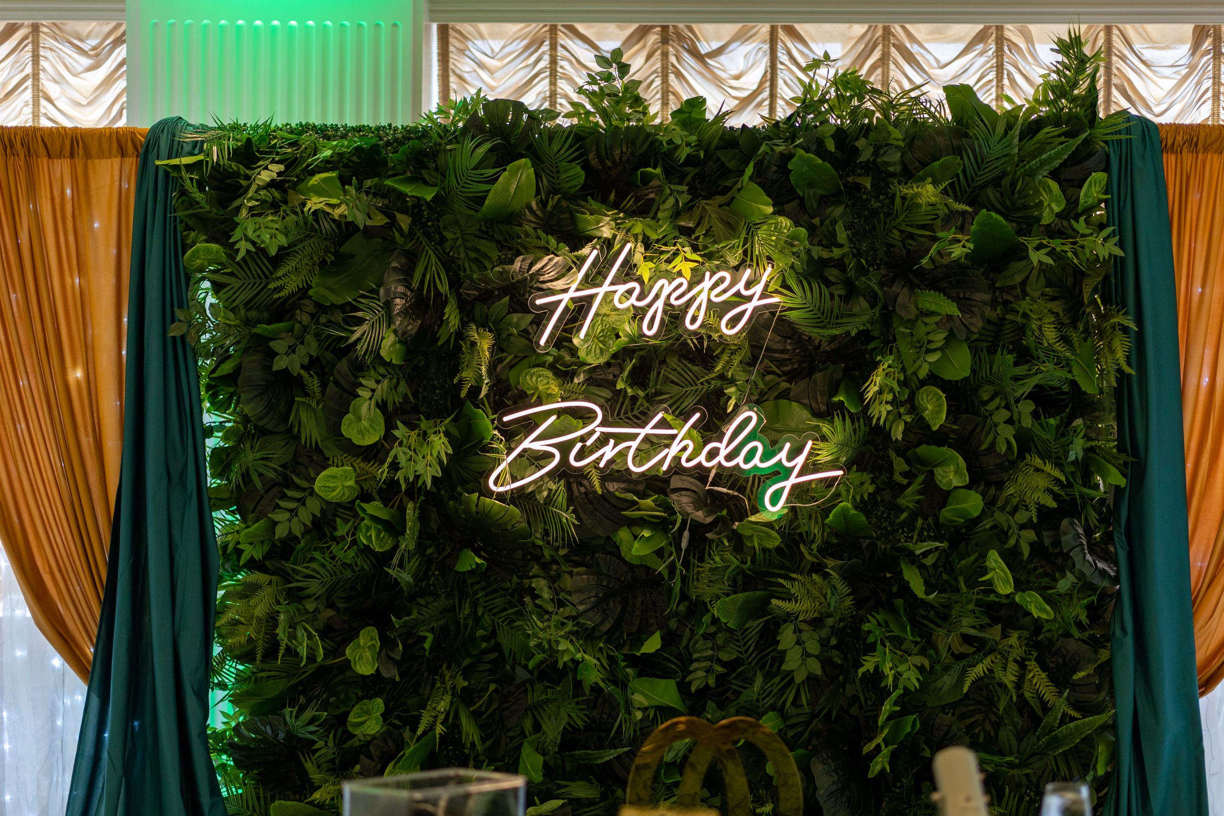 Green event backdrop with draped curtains and illuminated neon signs for a celebration.