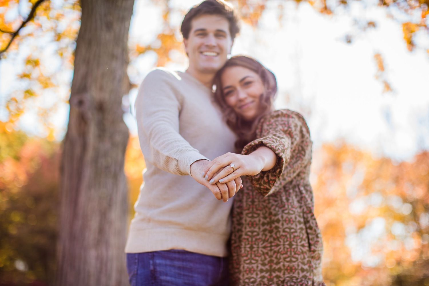 Couple embraces during sunset photoshoot with golden autumn trees in background.