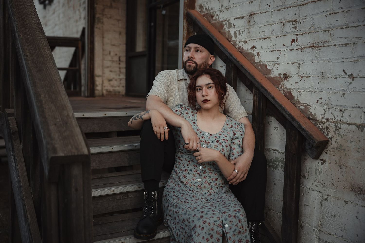 Romantic portrait of couple sitting on vintage wooden staircase against white brick wall.