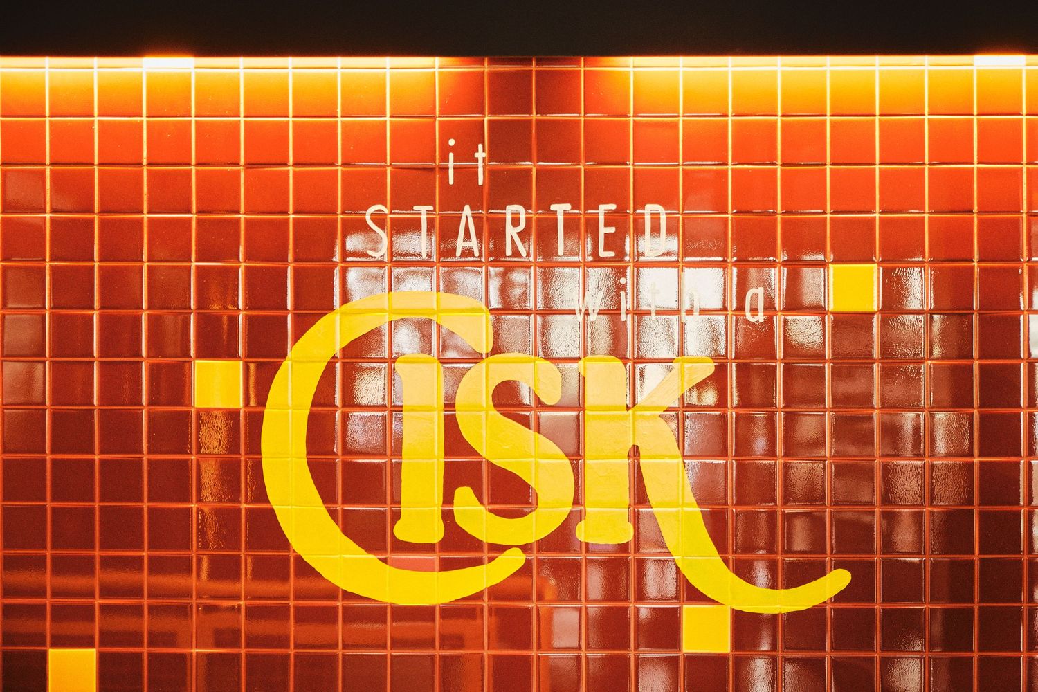 Orange-lit tiled wall displaying illuminated Cisk beer branding at night.