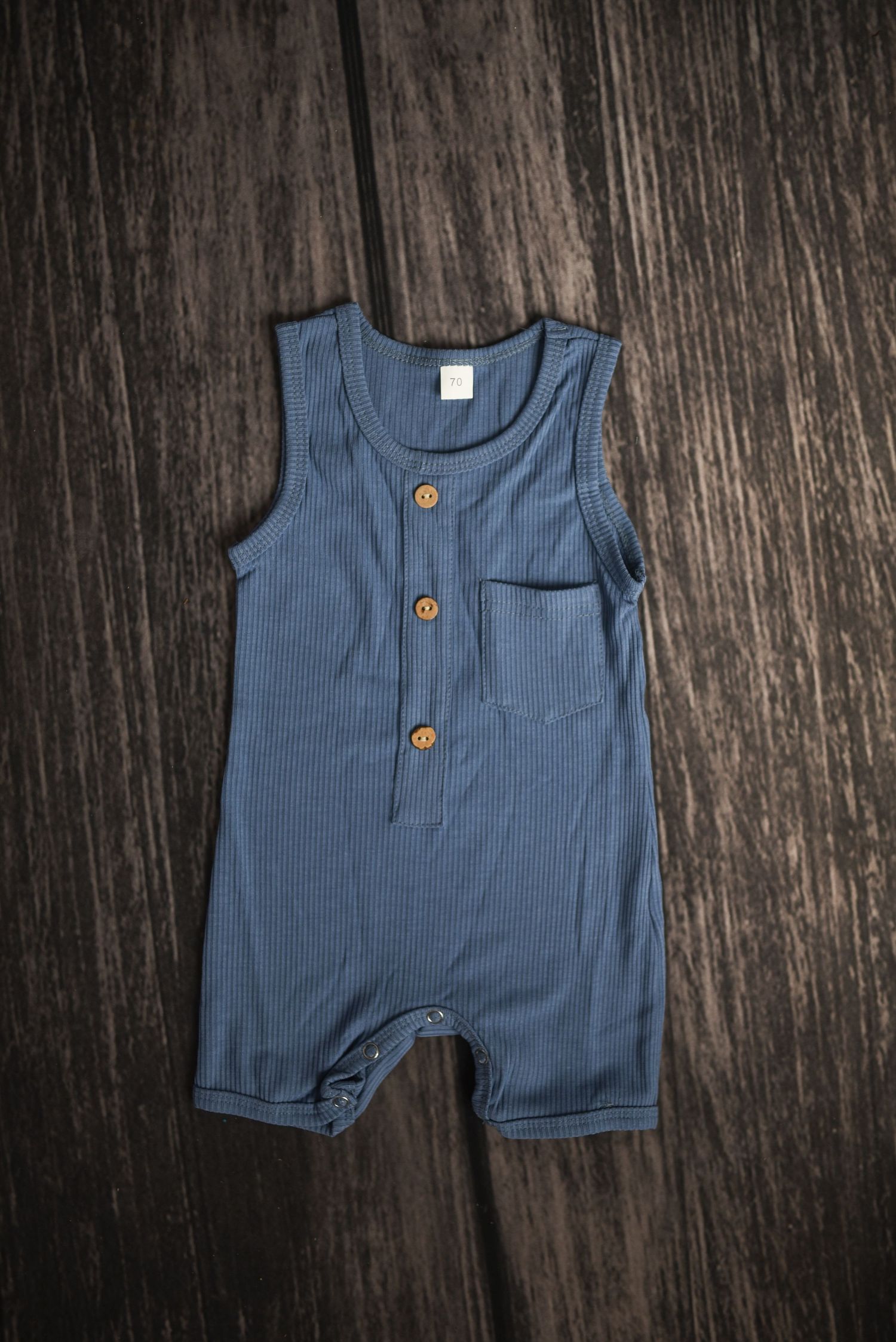 Blue ribbed baby romper with wooden buttons displayed on dark wooden surface.