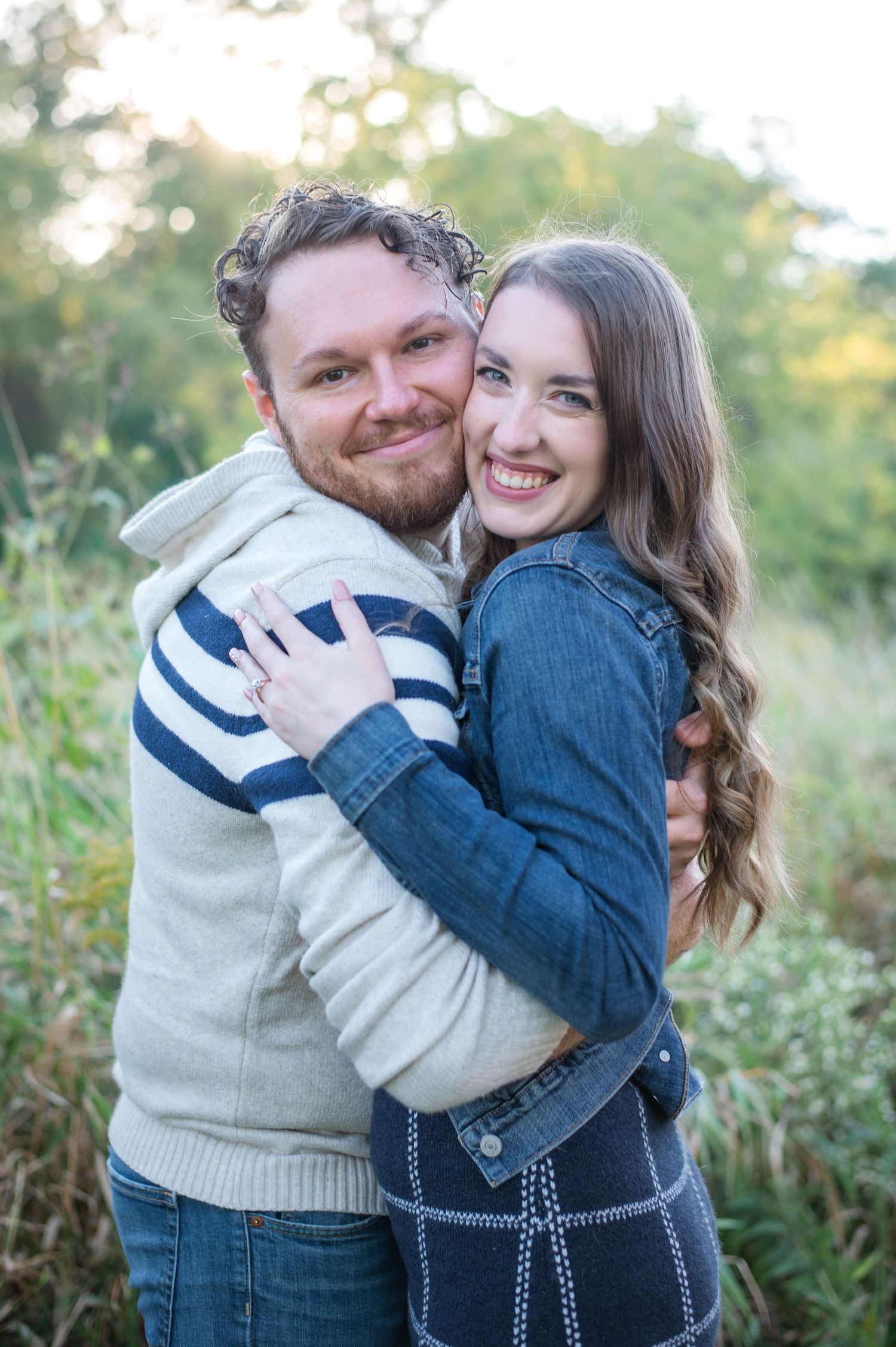 A couple embraces while smiling outdoors in casual sweaters.