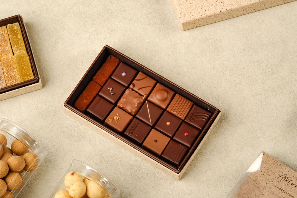 An elegant box of assorted artisan chocolates with varied shapes and flavors arranged in a grid.
