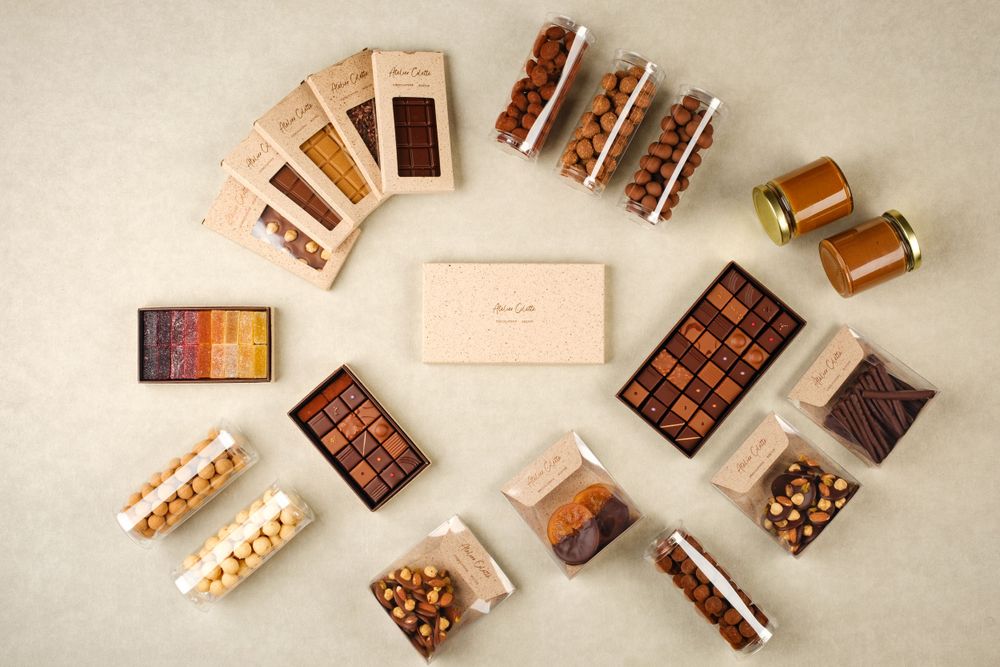 Atelier Colette luxury chocolate collection flatlay with bars, bonbons, caramel jars and nuts.