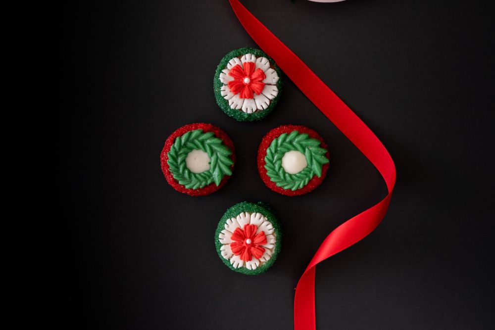 Four festive Christmas cupcakes decorated with green and red frosting and a red ribbon on black.