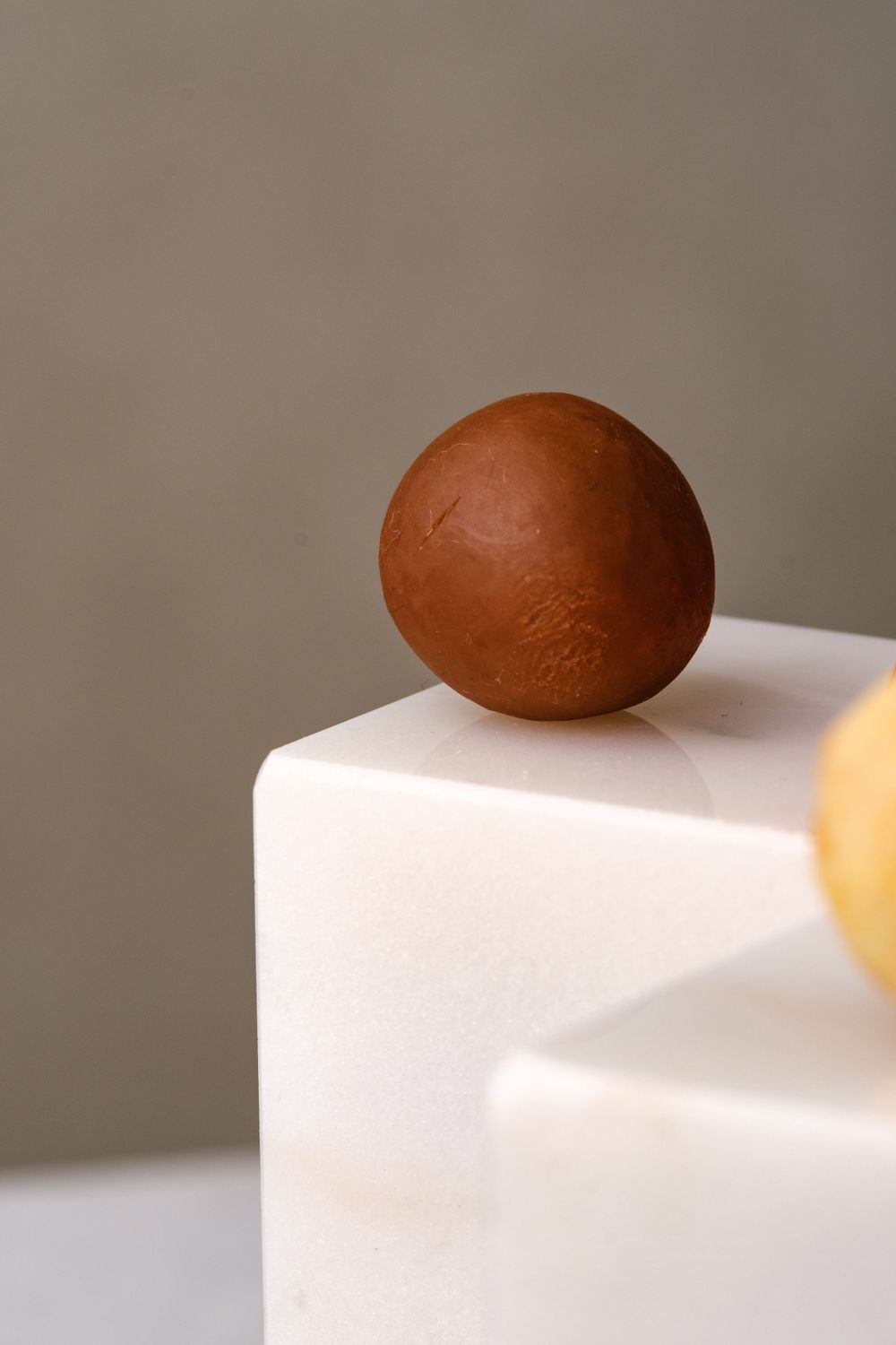 A smooth round milk chocolate truffle ball placed on the edge of a white marble pedestal.