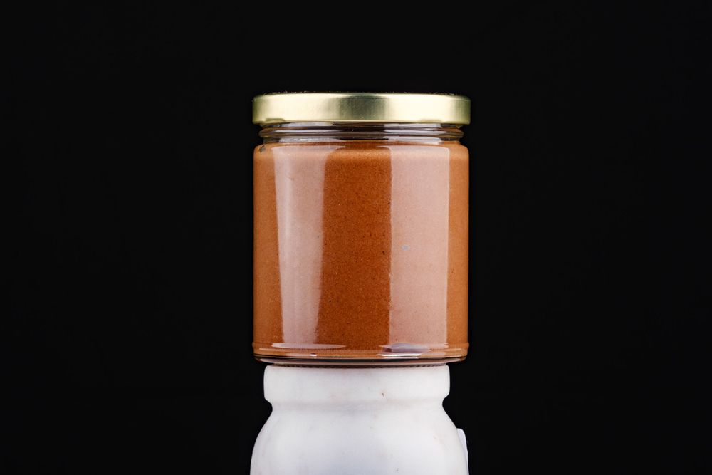 A glass jar with gold lid filled with smooth caramel spread against a dark background.