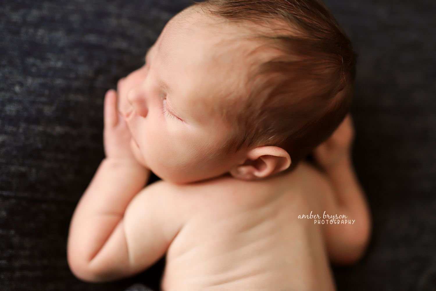 Side view of sleeping newborn against dark textured background.