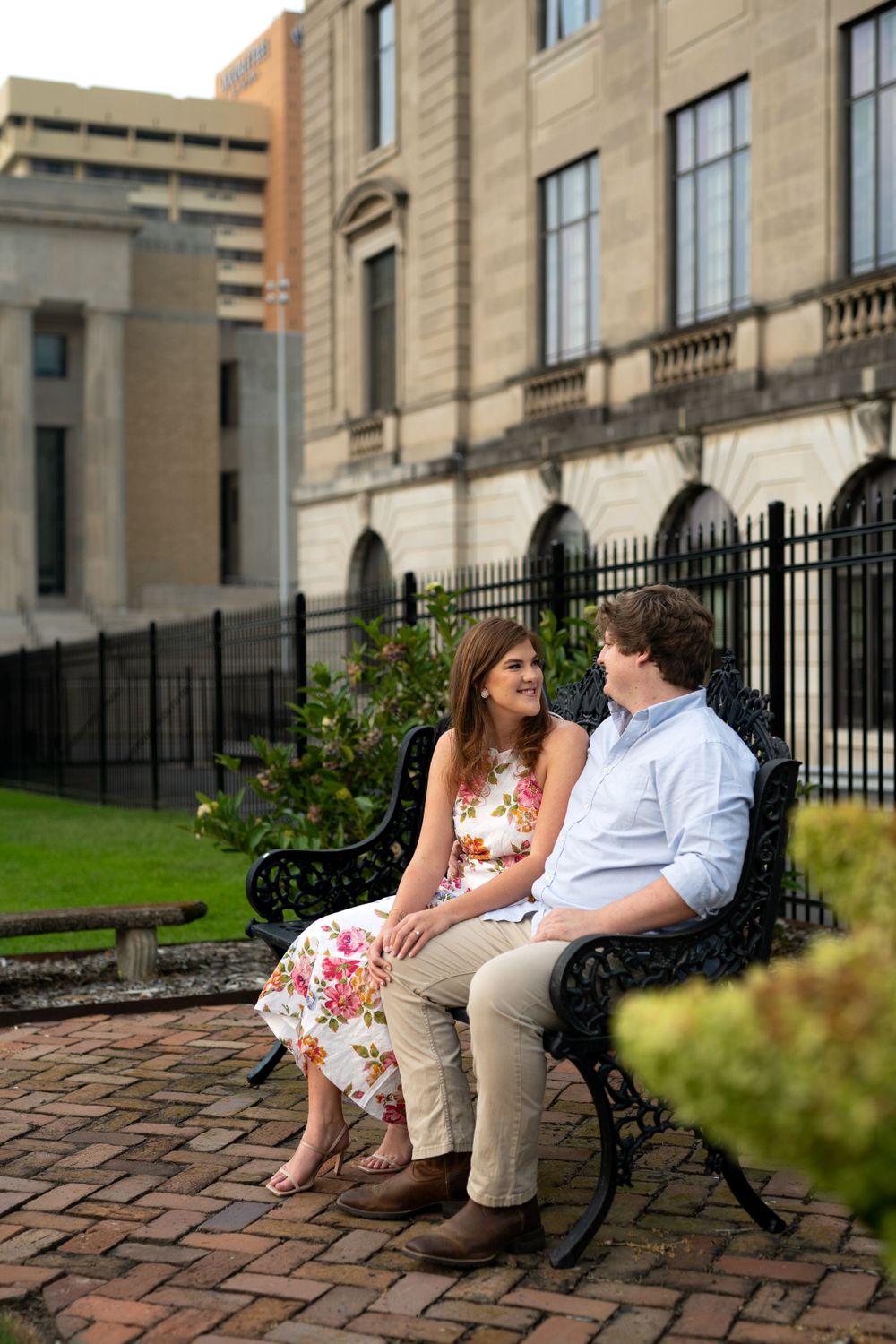 Couple sitting on a bench outside a historic stone building with iron fencing.