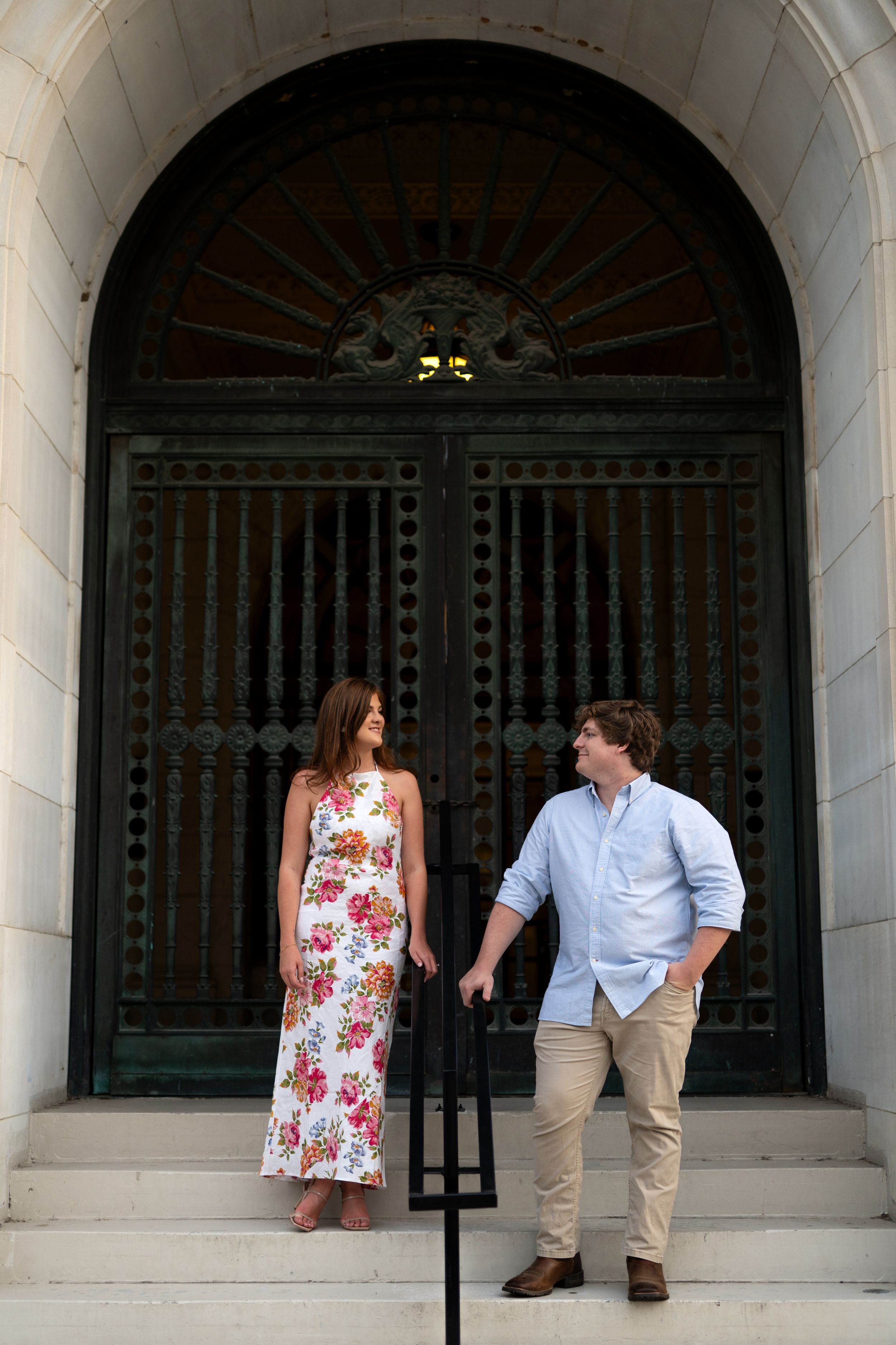 Couple posing playfully under stone archways of a classic building.