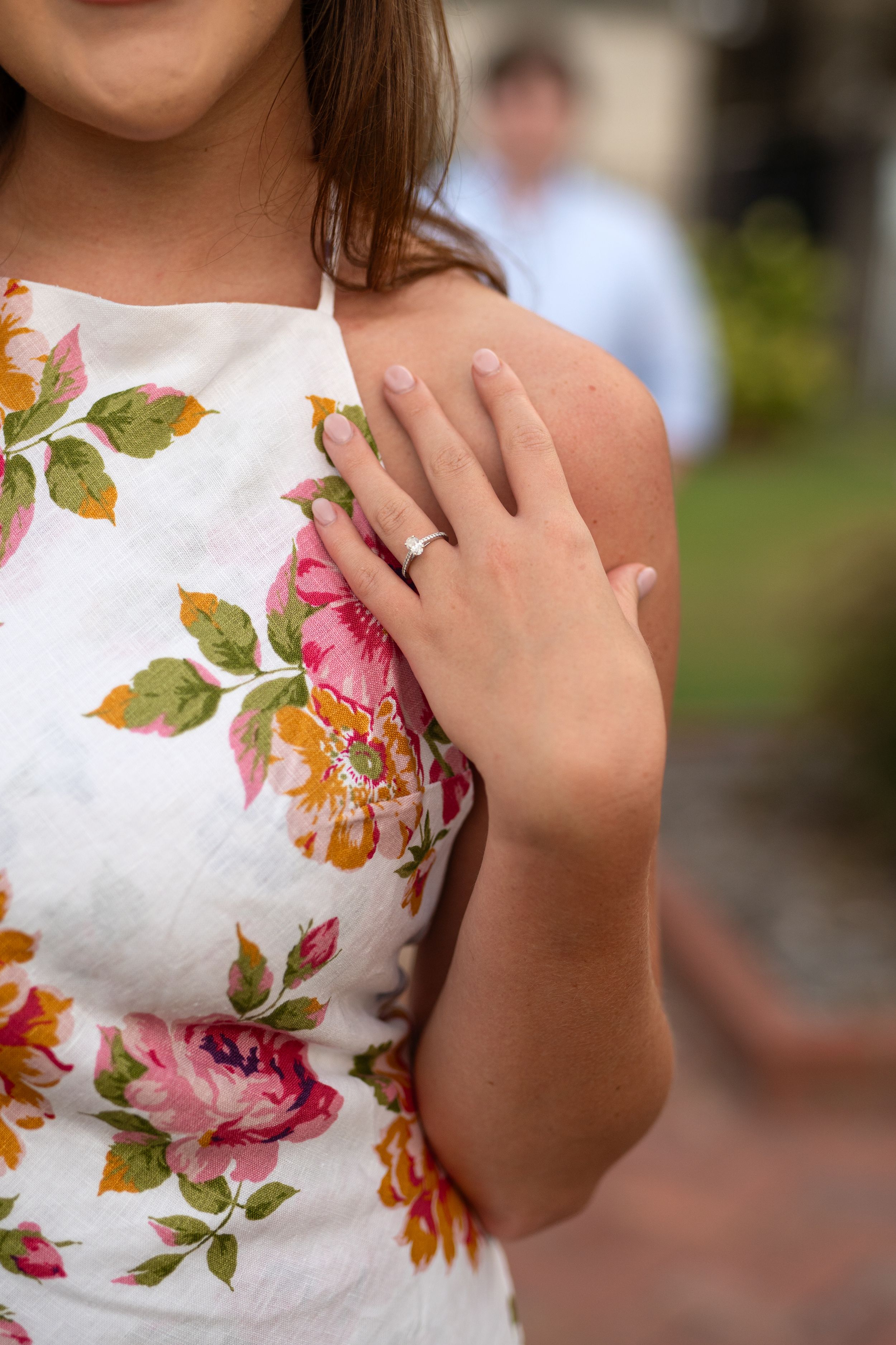 Close-up details of a floral white dress and engagement ring.