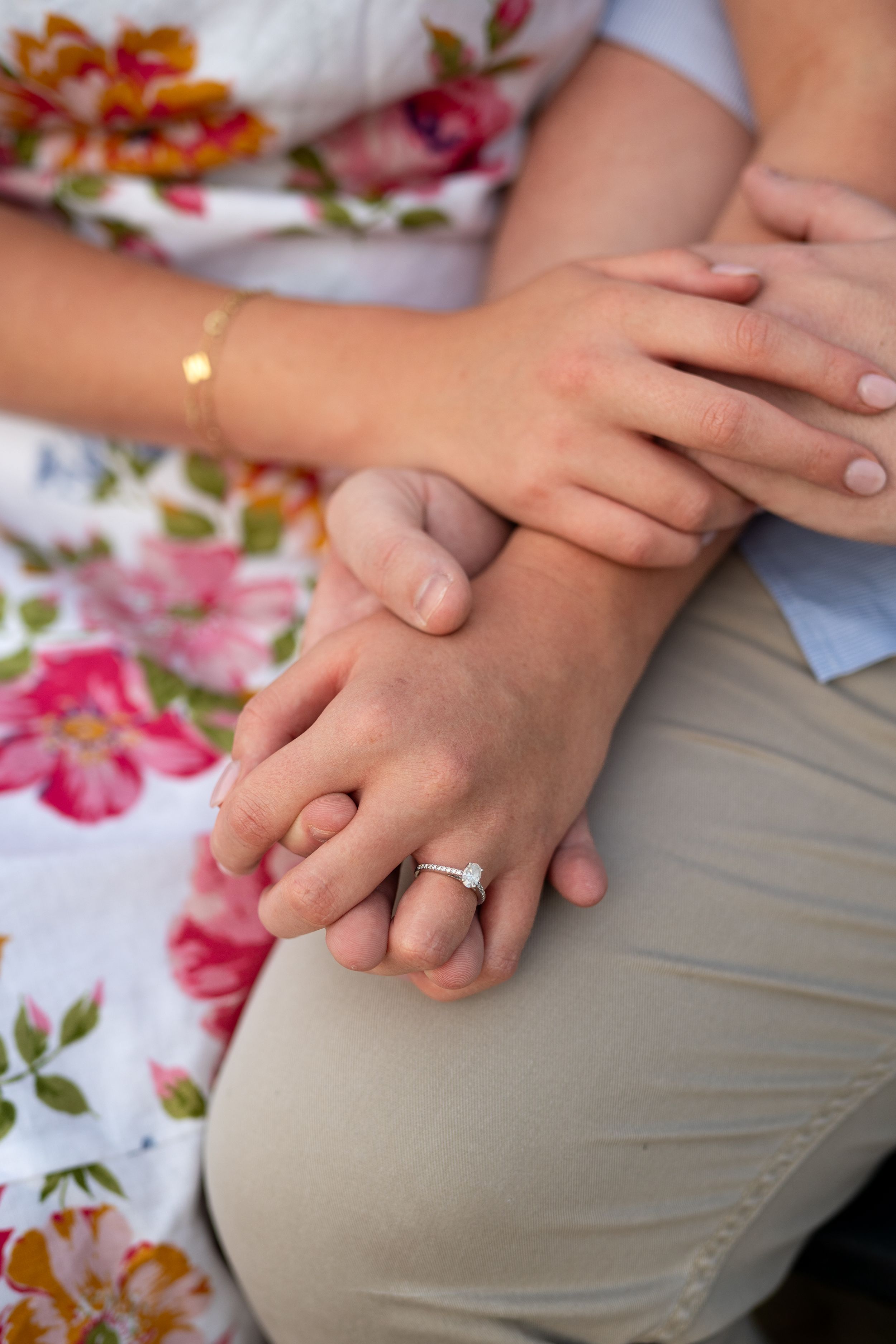 Close-up shot of clasped hands showing an engagement ring against a floral tablecloth.