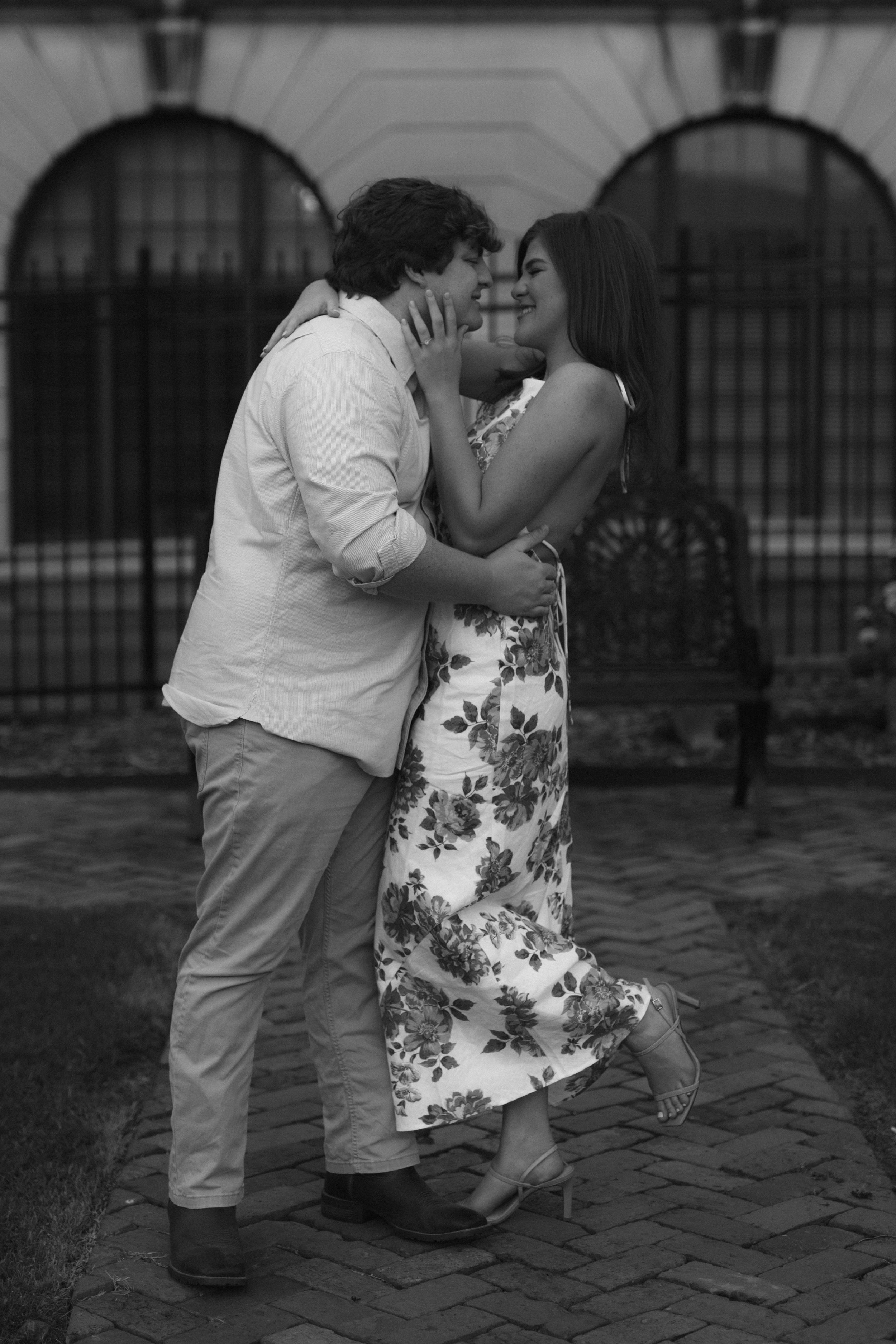 Black and white photo of a couple sharing a romantic moment on brick pavement.