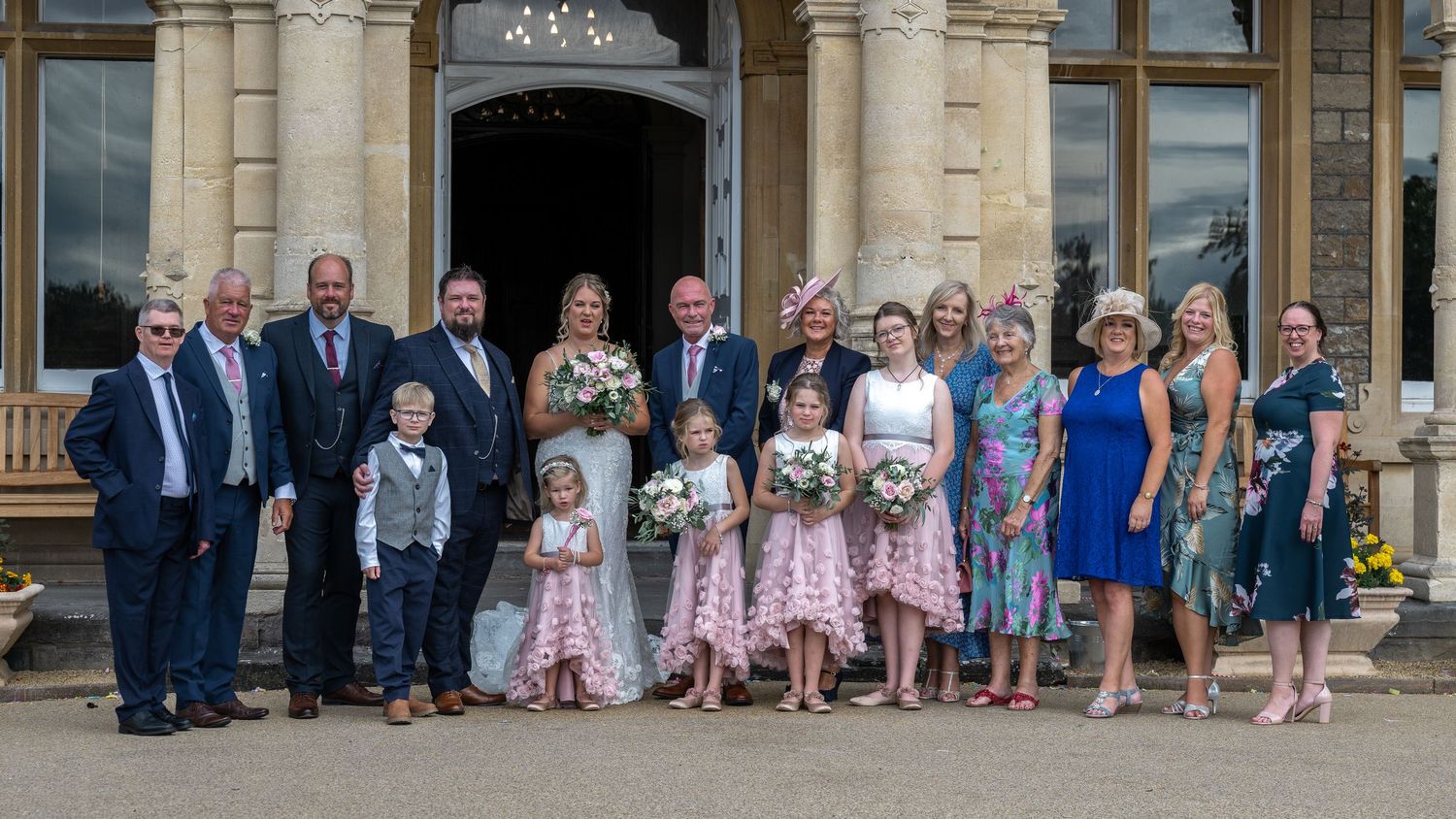 Wedding party and guests posed for formal group photo in front of elegant stone mansion.