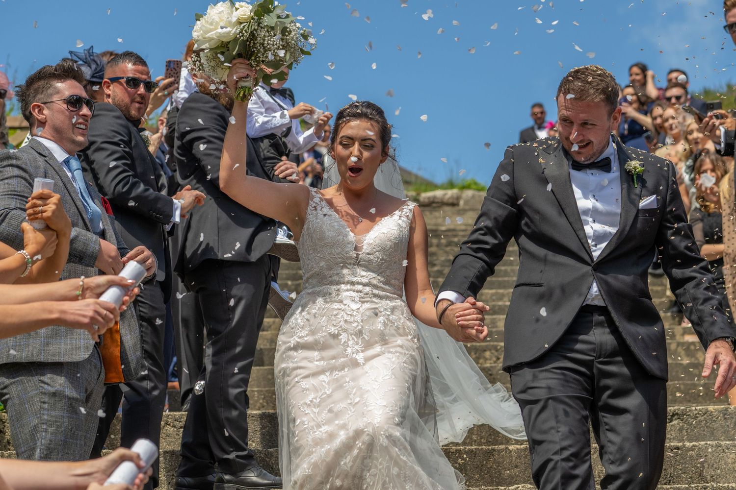 Joyful celebration with confetti being thrown on outdoor stone steps during wedding festivities.