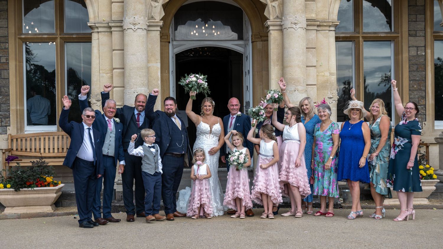 Celebratory group photo of wedding party and guests on grand steps of historic building.