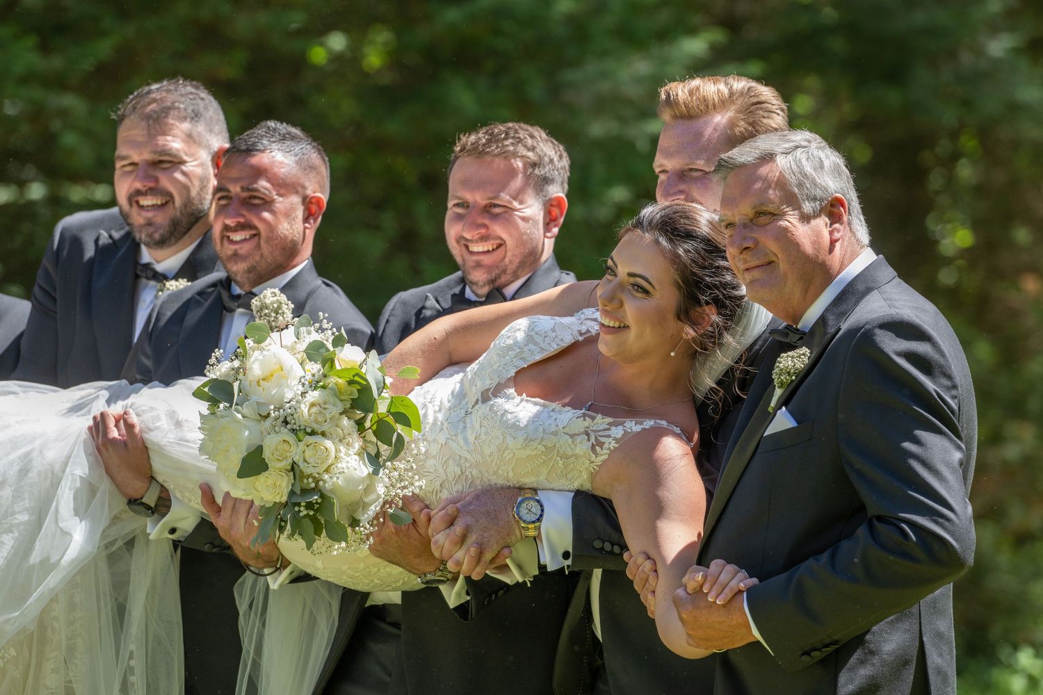 Wedding party laughing together while posing with white floral bouquets outdoors.
