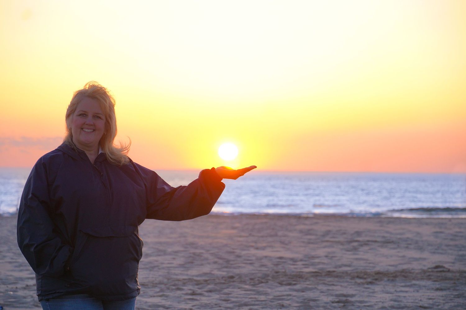 Person holding the setting sun at golden hour on a beach.